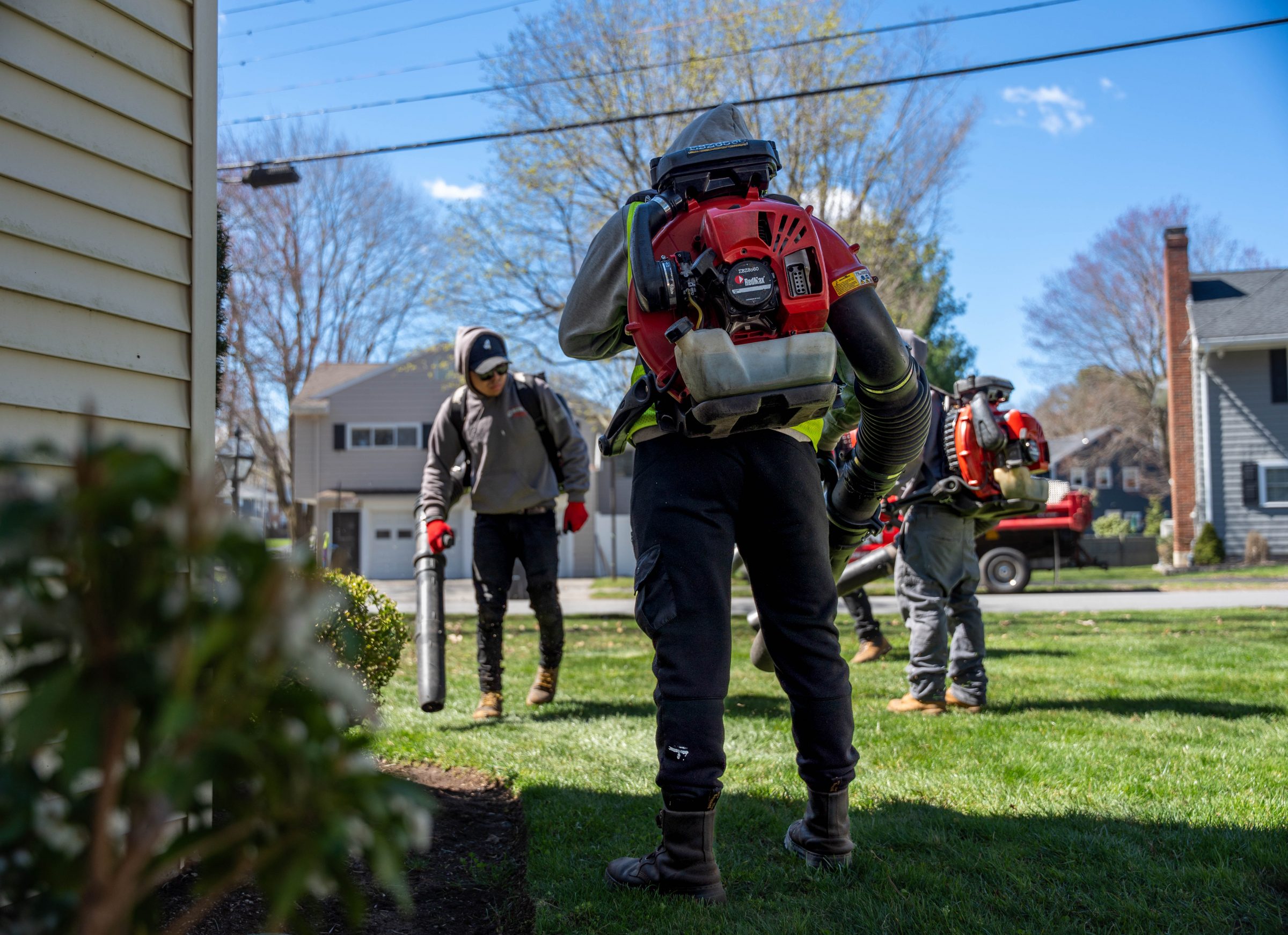 Landscapers using backpack leaf blowers on suburban lawn