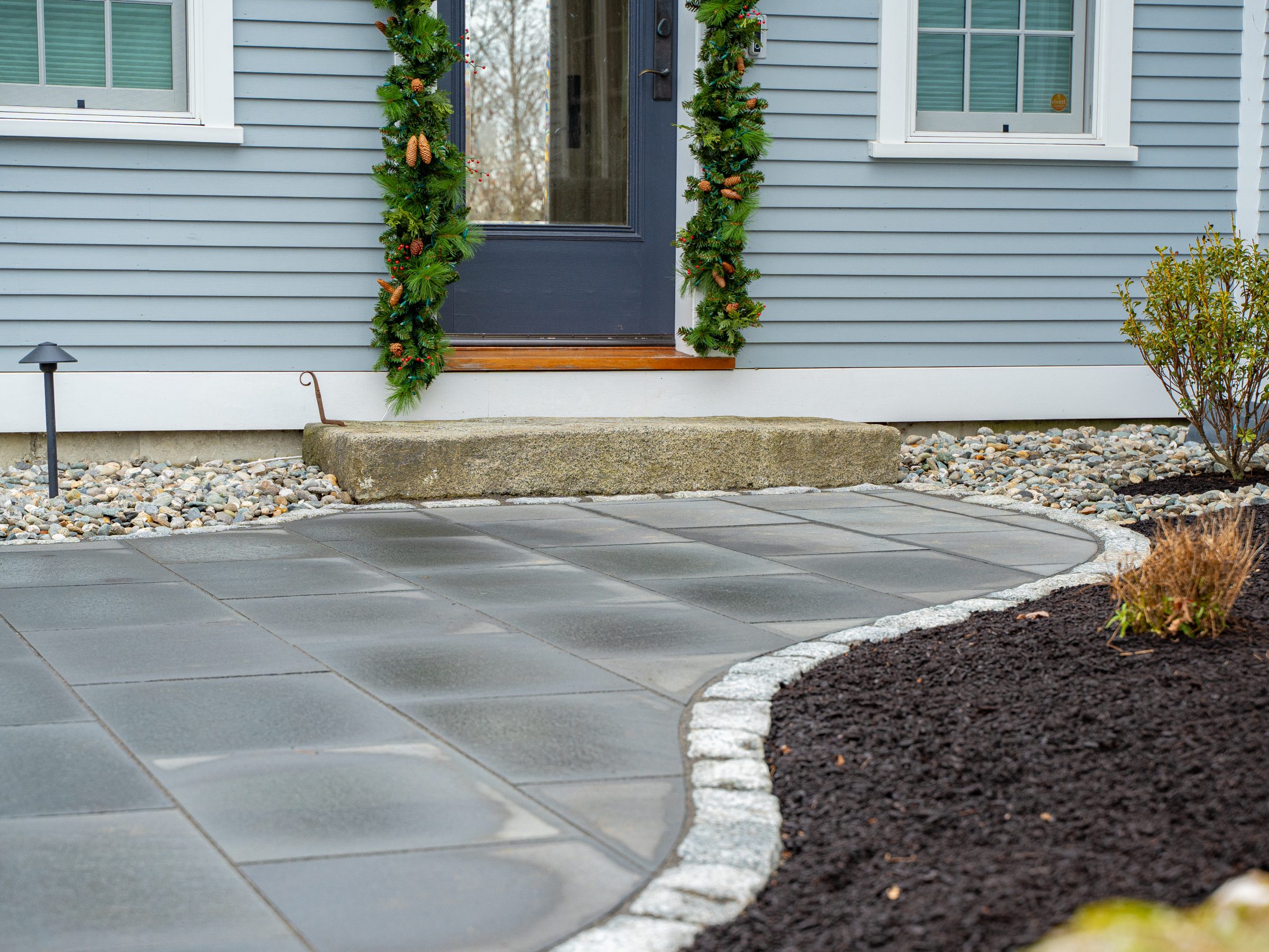 Front door with garland and stone walkway