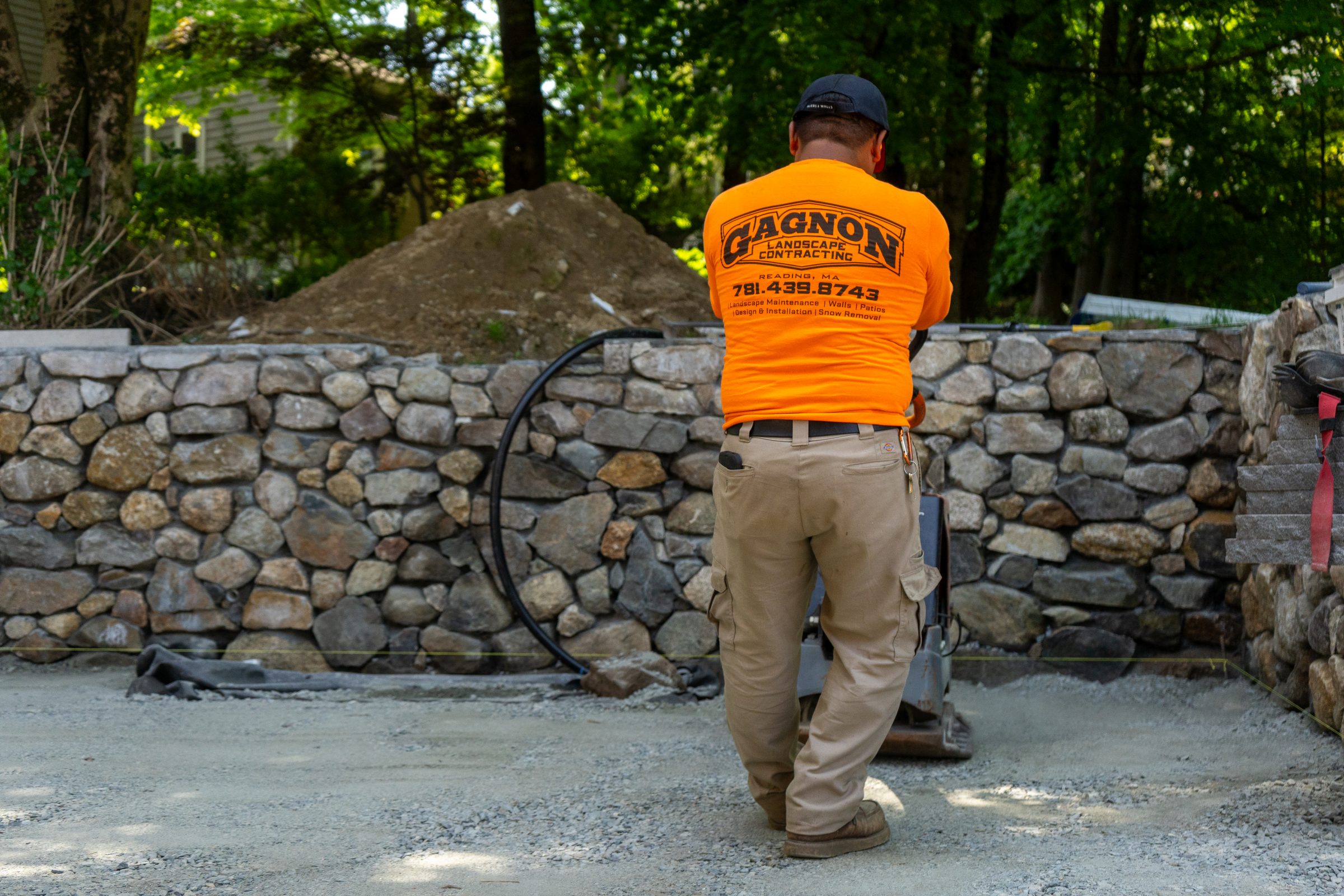 Landscaper compacting gravel near stone retaining wall