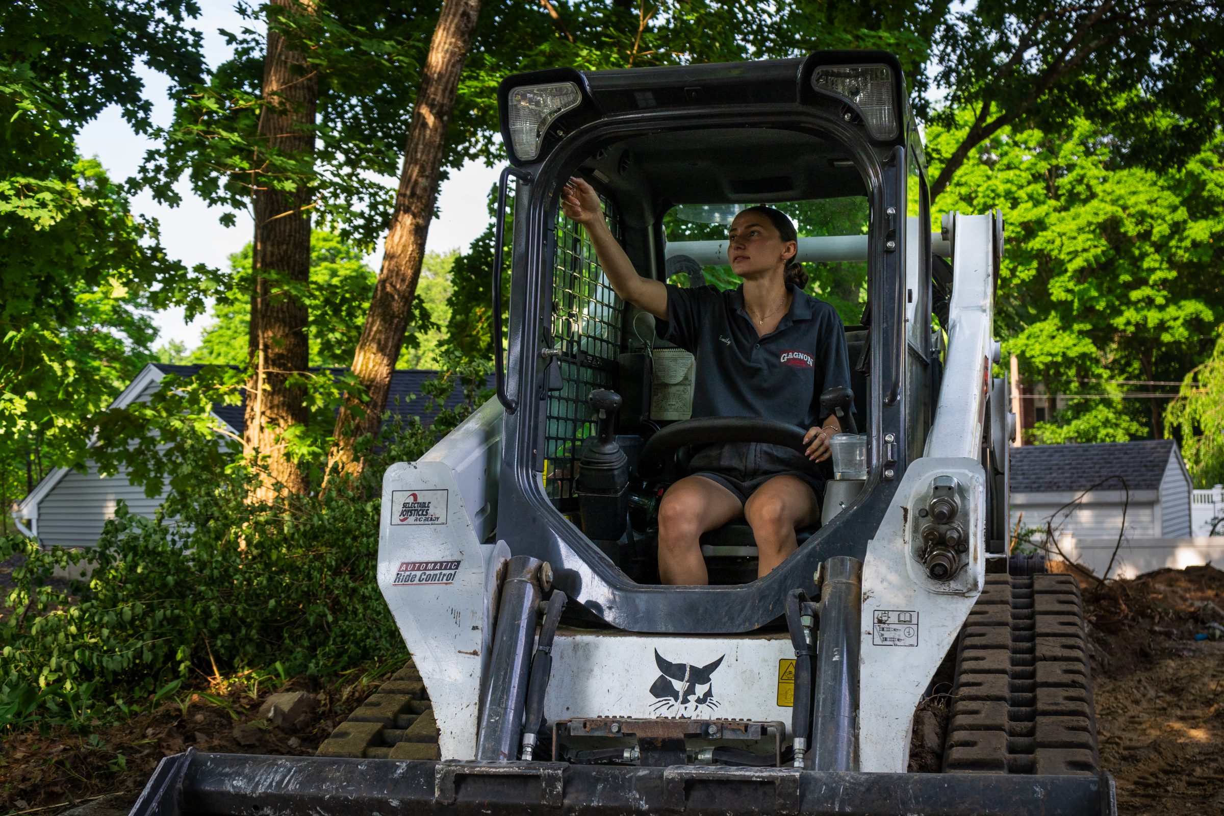 Woman operating skid-steer loader in wooded yard