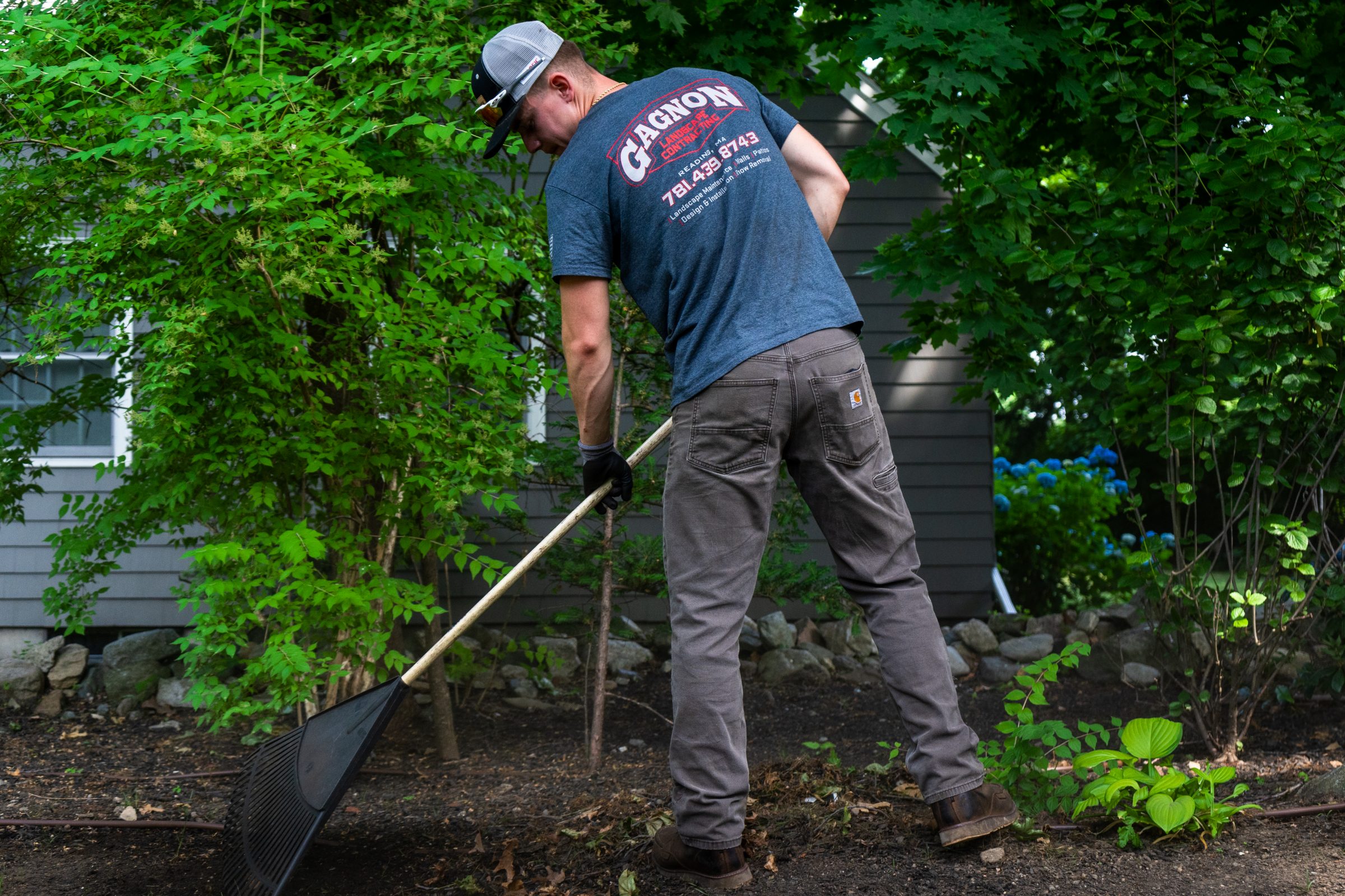 Landscaper raking garden bed beside house