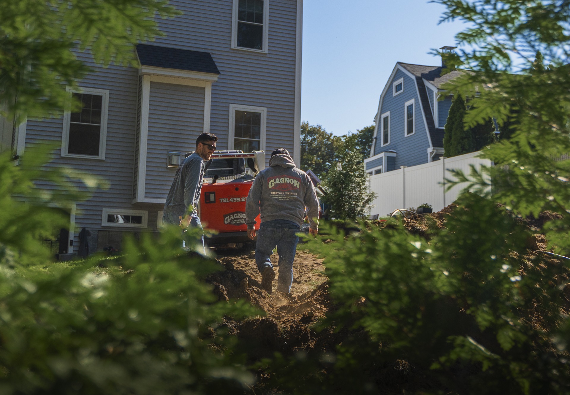 Workers digging trench with excavator in backyard