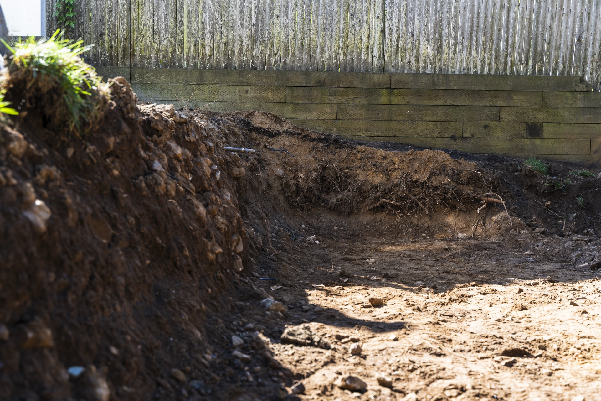 Large excavated backyard hole near wooden fence
