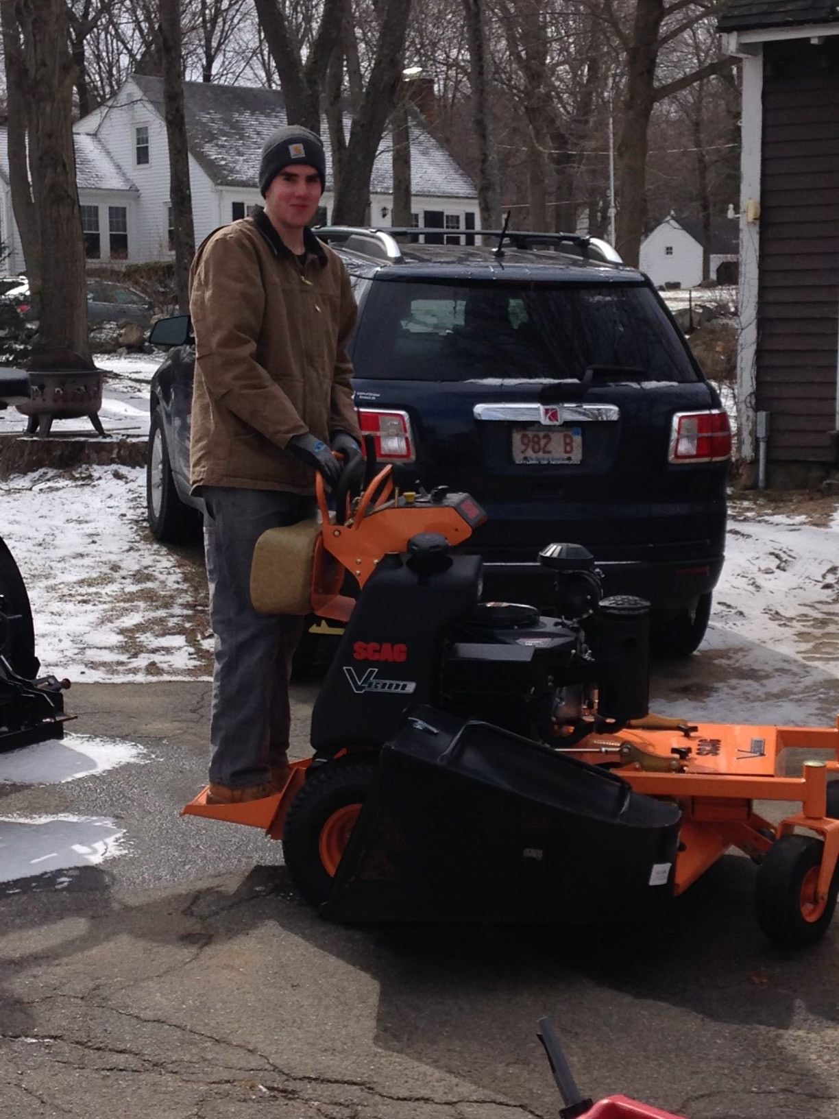 Man standing on orange lawn mower in driveway