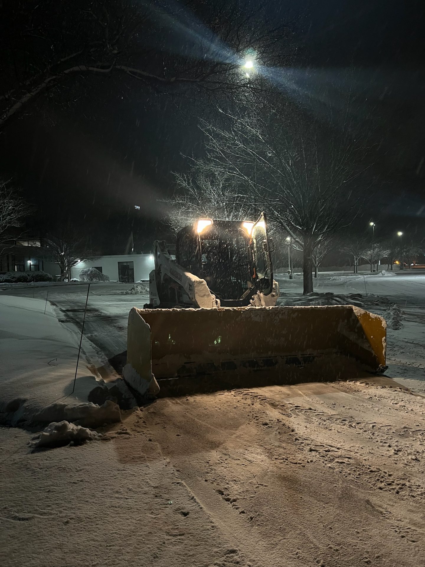 Snowplow clearing parking lot at night snowfall