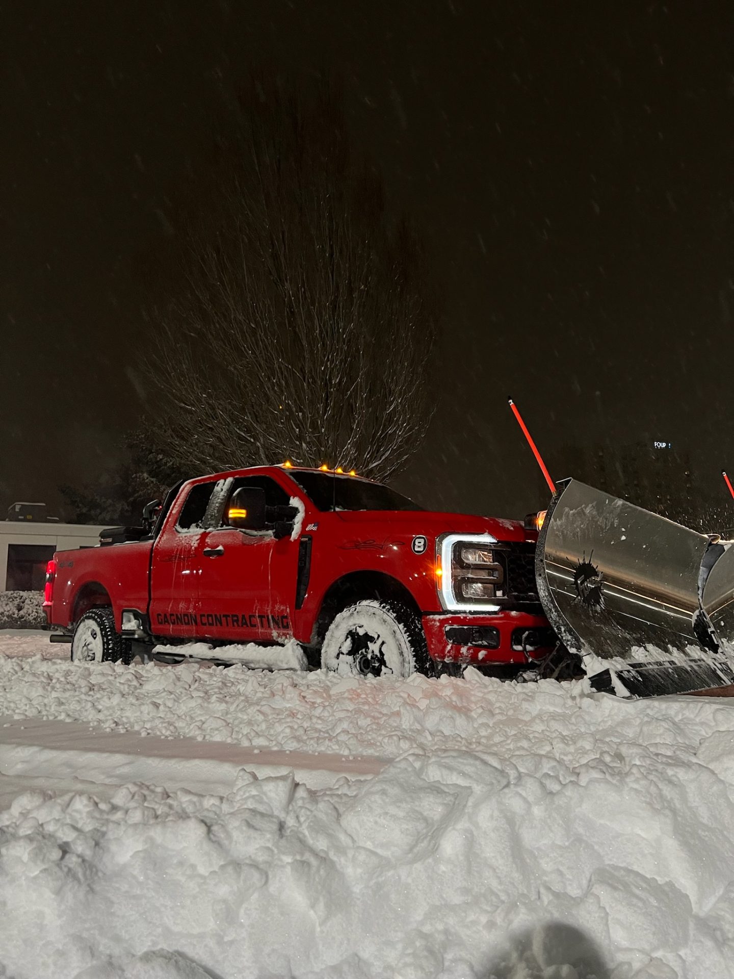 Red pickup truck plowing snow at night