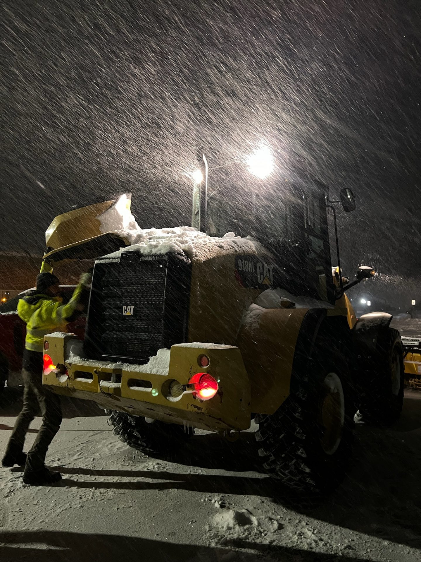 Worker clearing snow off CAT telehandler at night