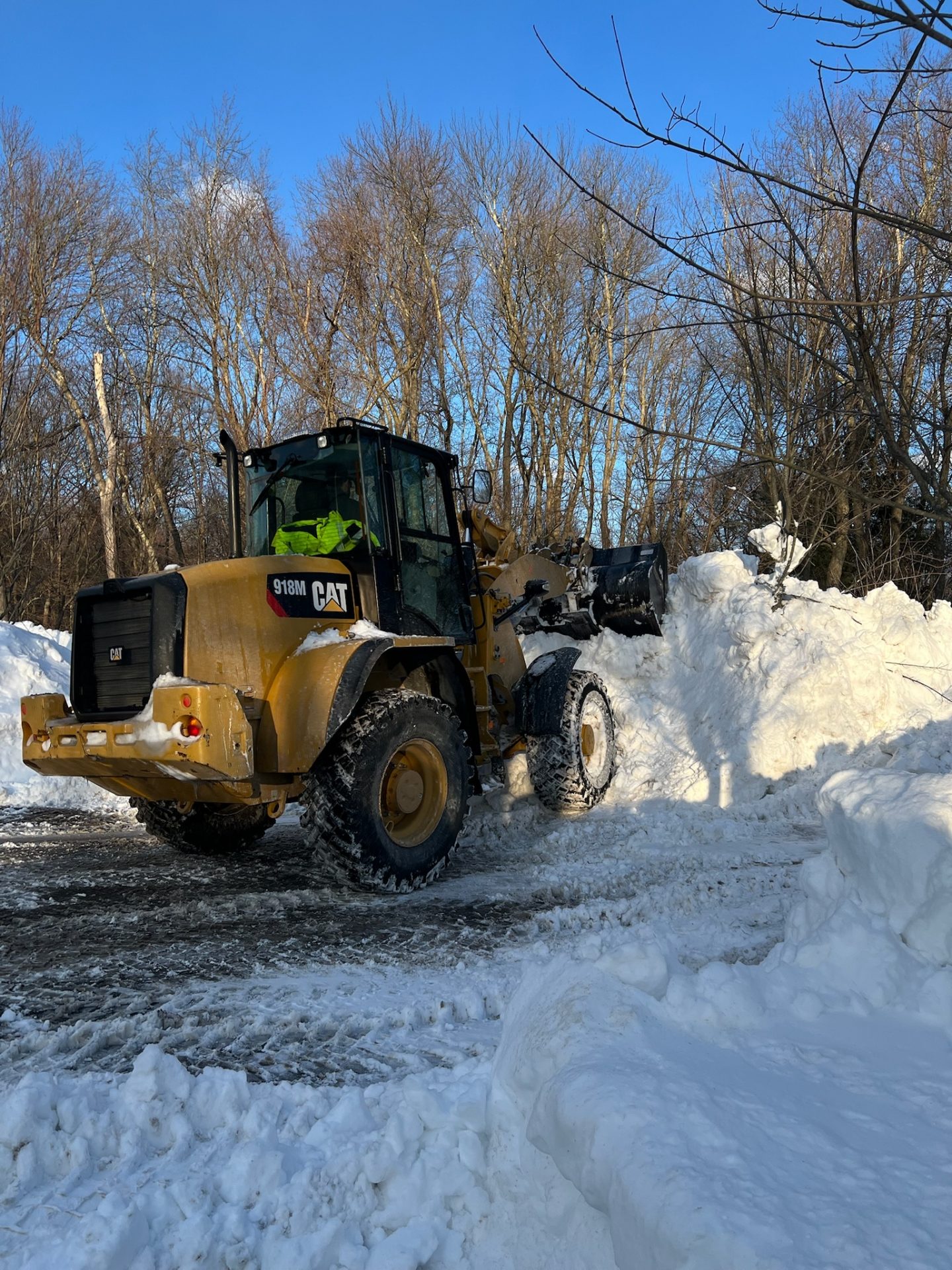 Front loader clearing snow beside wooded road