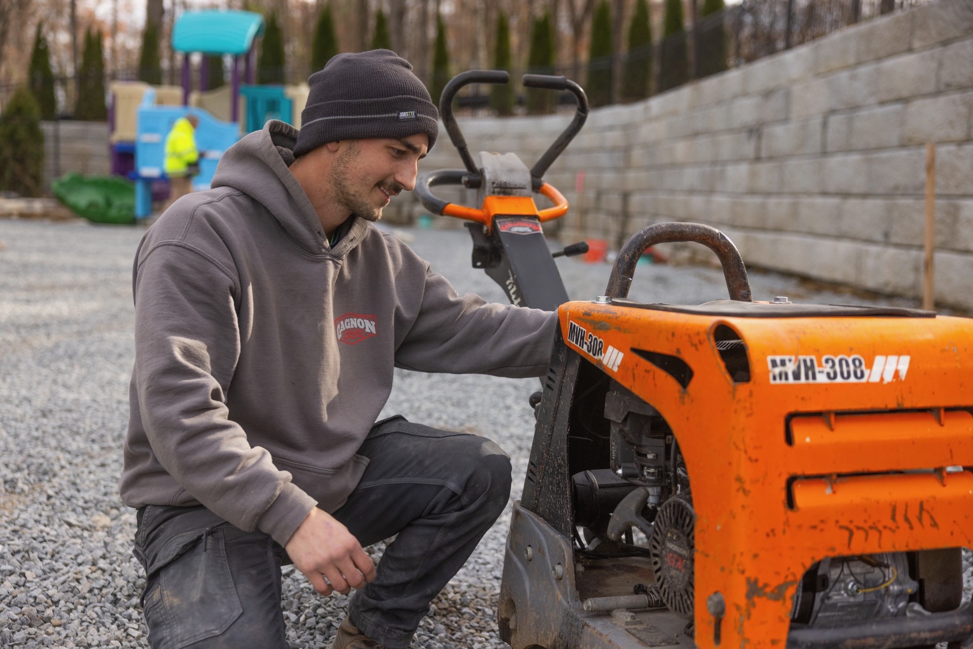 Man inspecting orange plate compactor on gravel