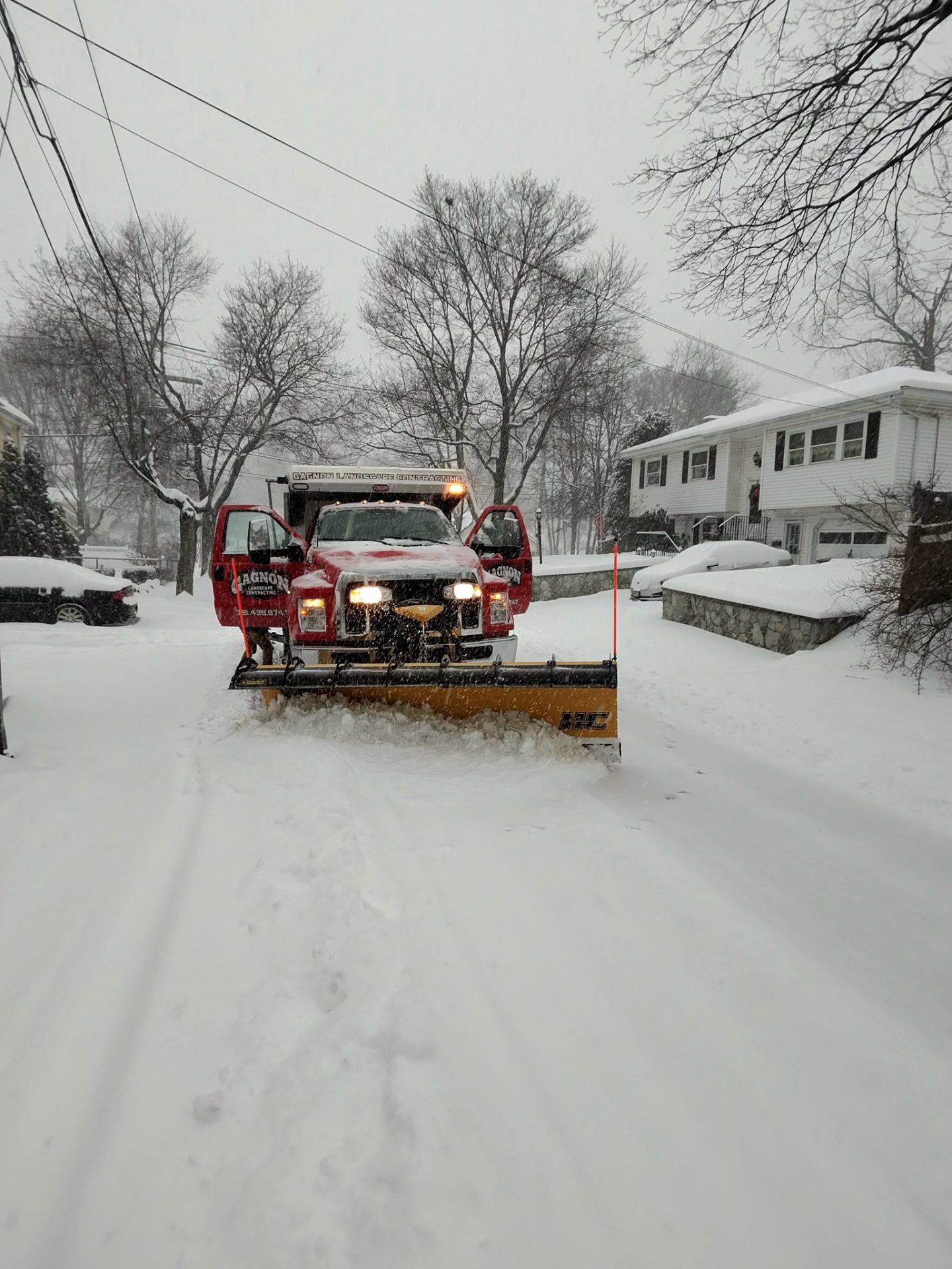 Red snowplow truck clearing residential driveway in snowstorm