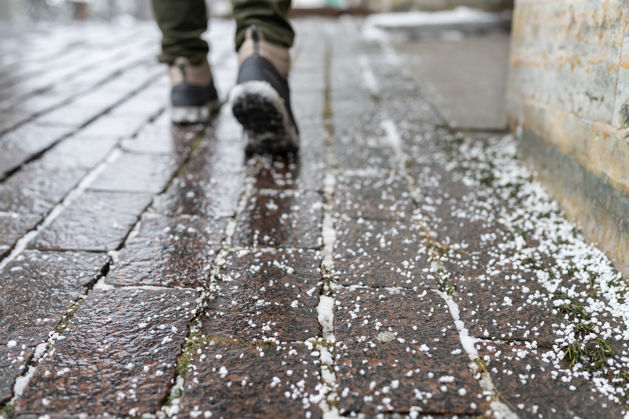 Person walking on hail-covered cobblestone sidewalk