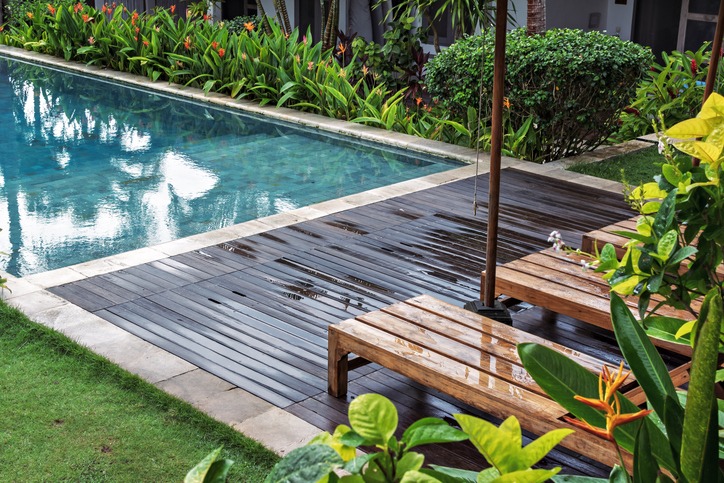 Tropical backyard pool with wooden deck chairs